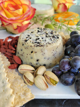 Load image into Gallery viewer, Close up image of a small cheese wheel with condiments, nuts, fruits, berries, crackers and flowers
