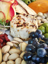 Load image into Gallery viewer, Close up image of small cheese wheel with pistachios, grapes, nuts, olives and flowers around it

