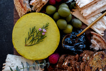 Load image into Gallery viewer, Close up image of yellow cheese wheel on cheese board with condiments 
