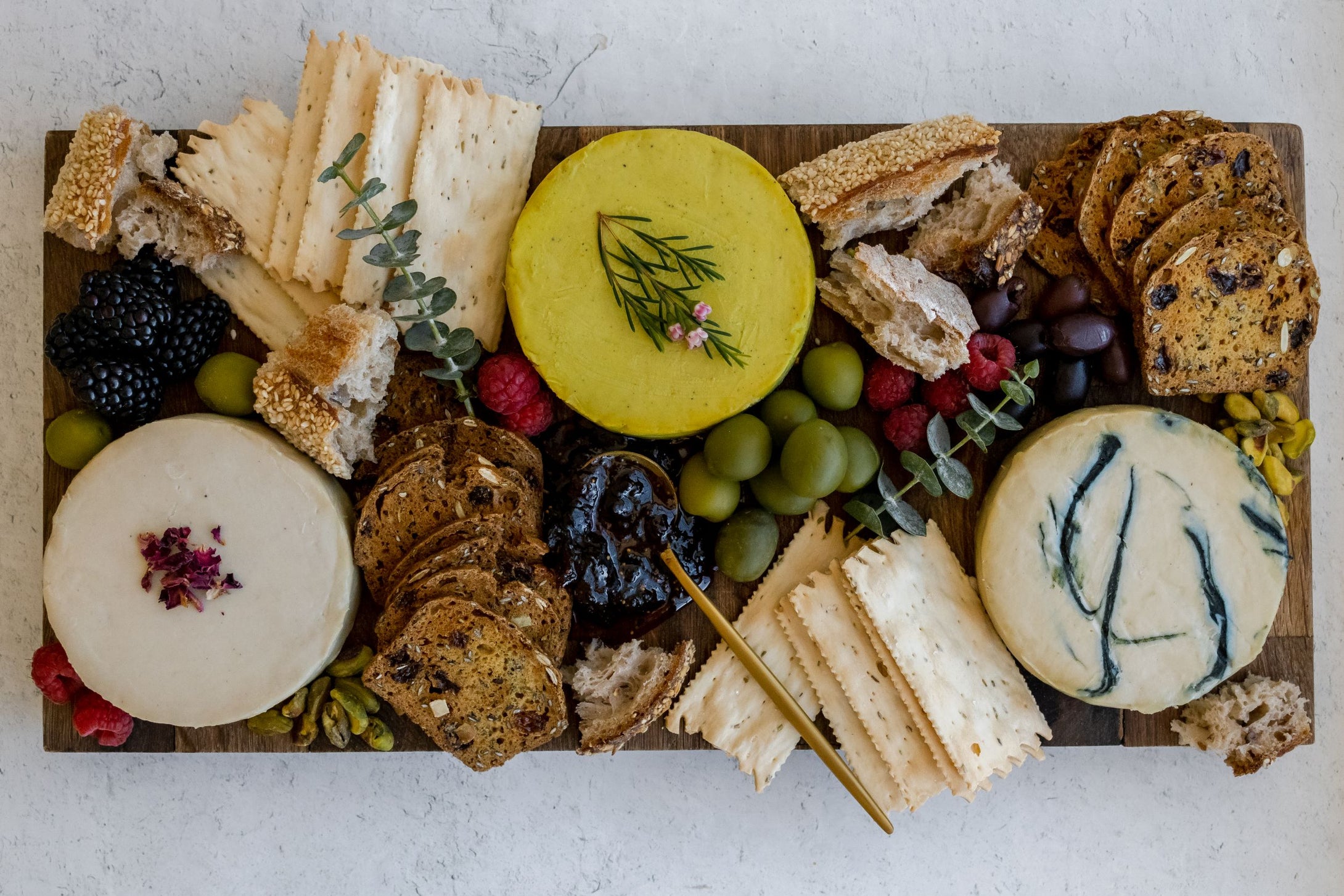 Bountiful cheese board with condiments, crackers and three cheese wheels seen from above